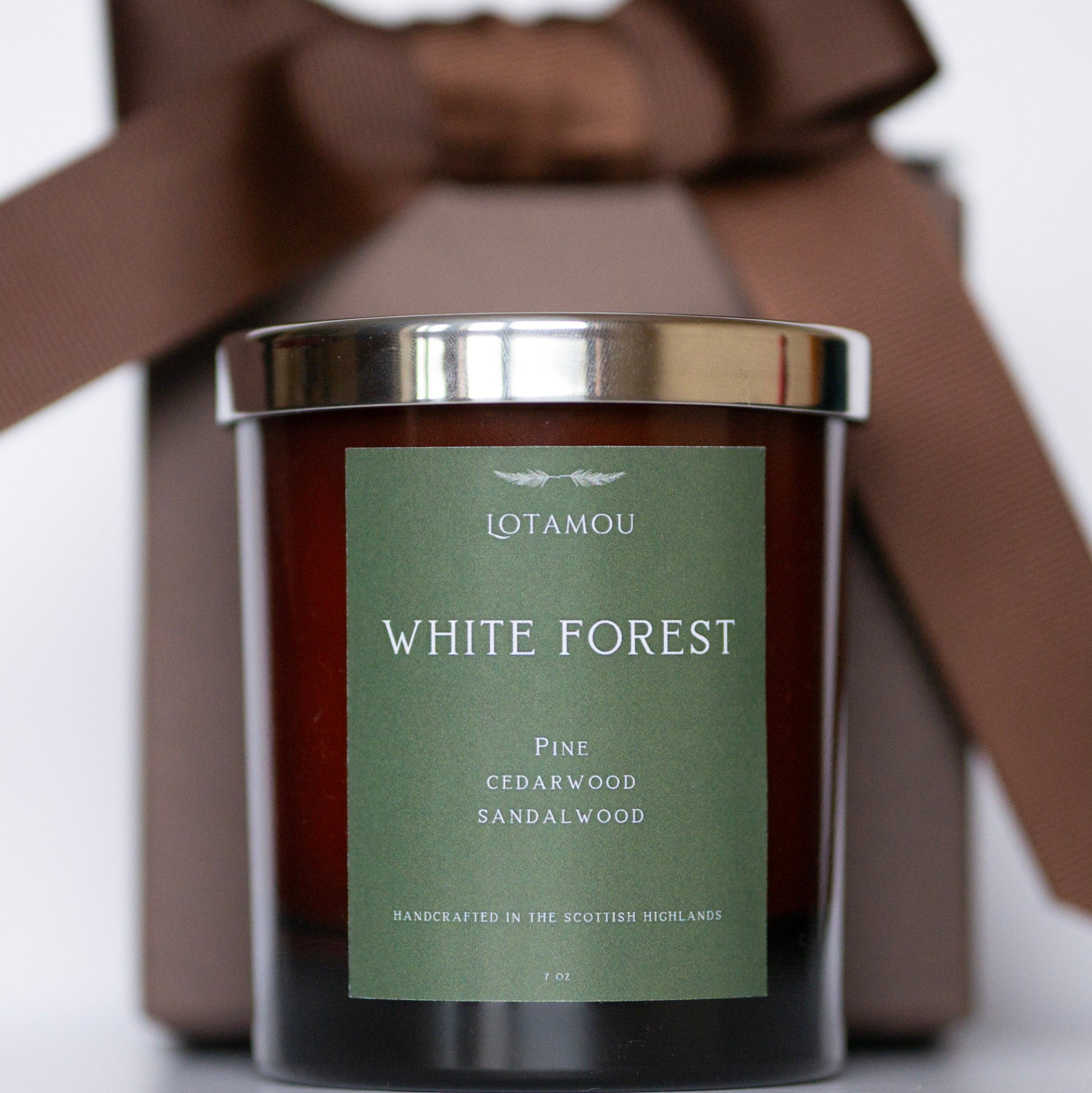 Candle with 'White Forest' label and brown bow in the background