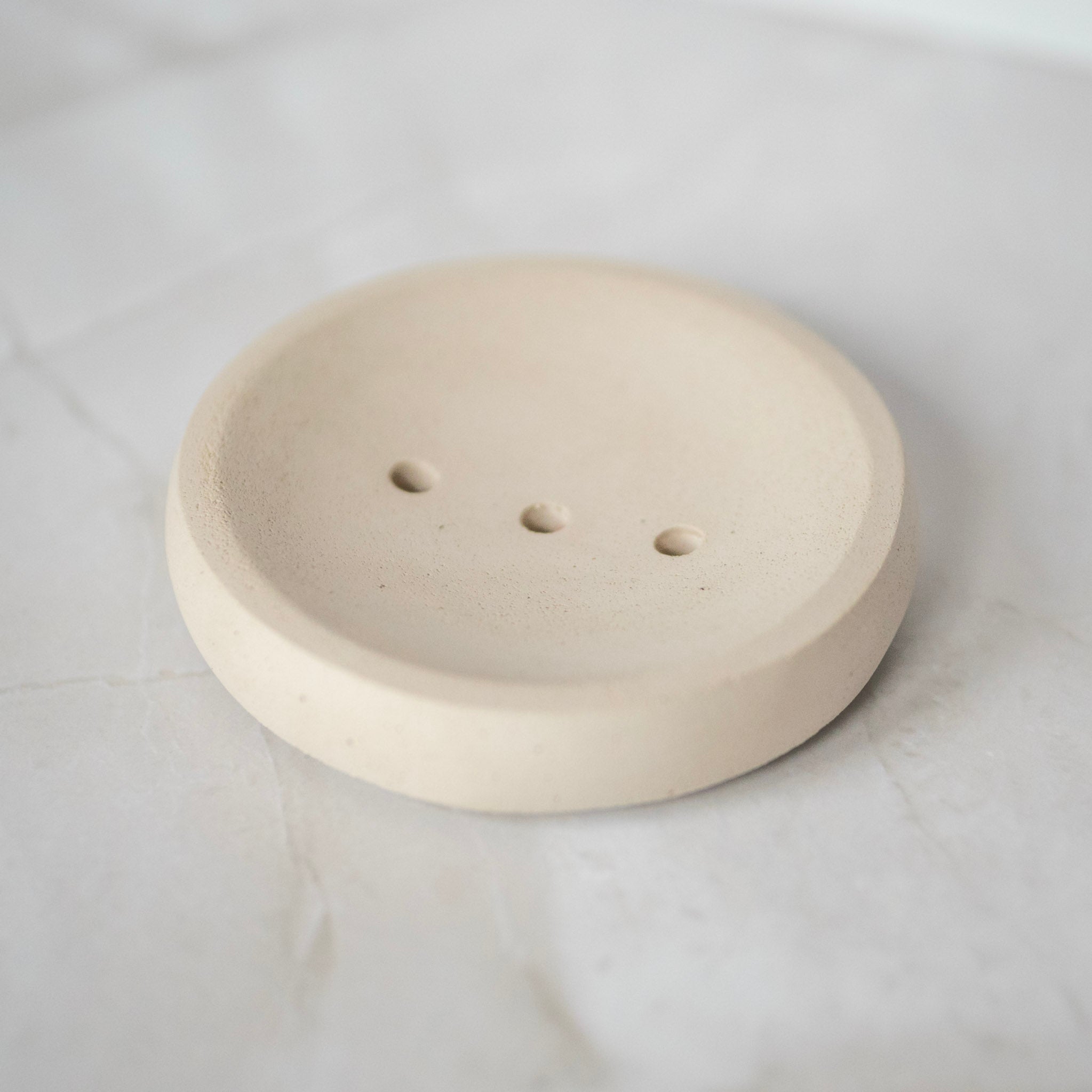 Round beige ceramic object with three small holes on a light gray background