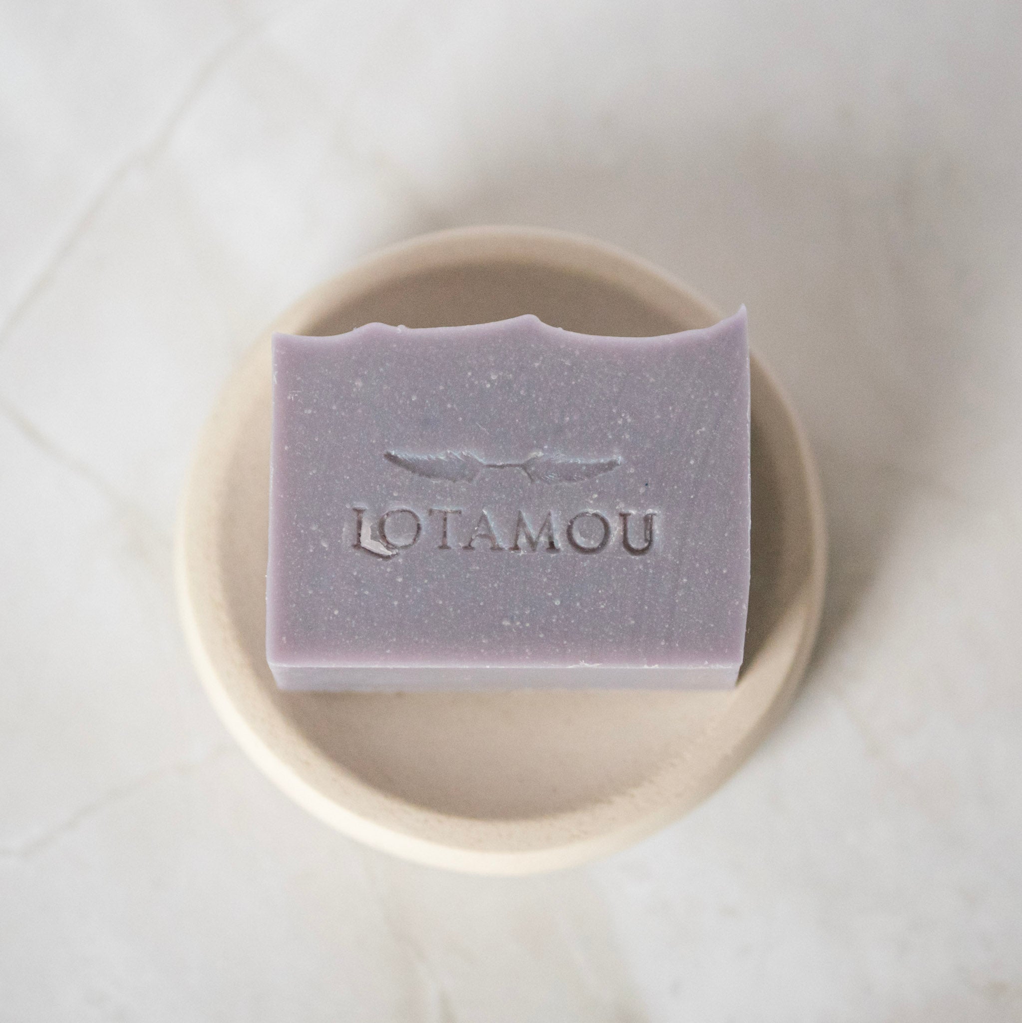 Purple soap bar with 'LOTAMOU' branding on a white plate.