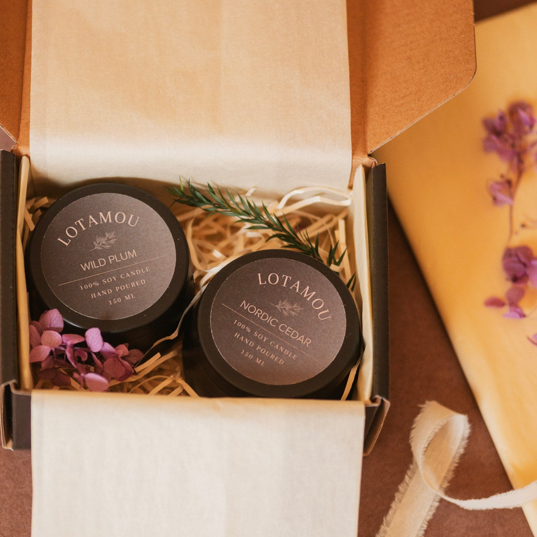Two Lotamou candles in a decorative box with flowers and a ribbon.