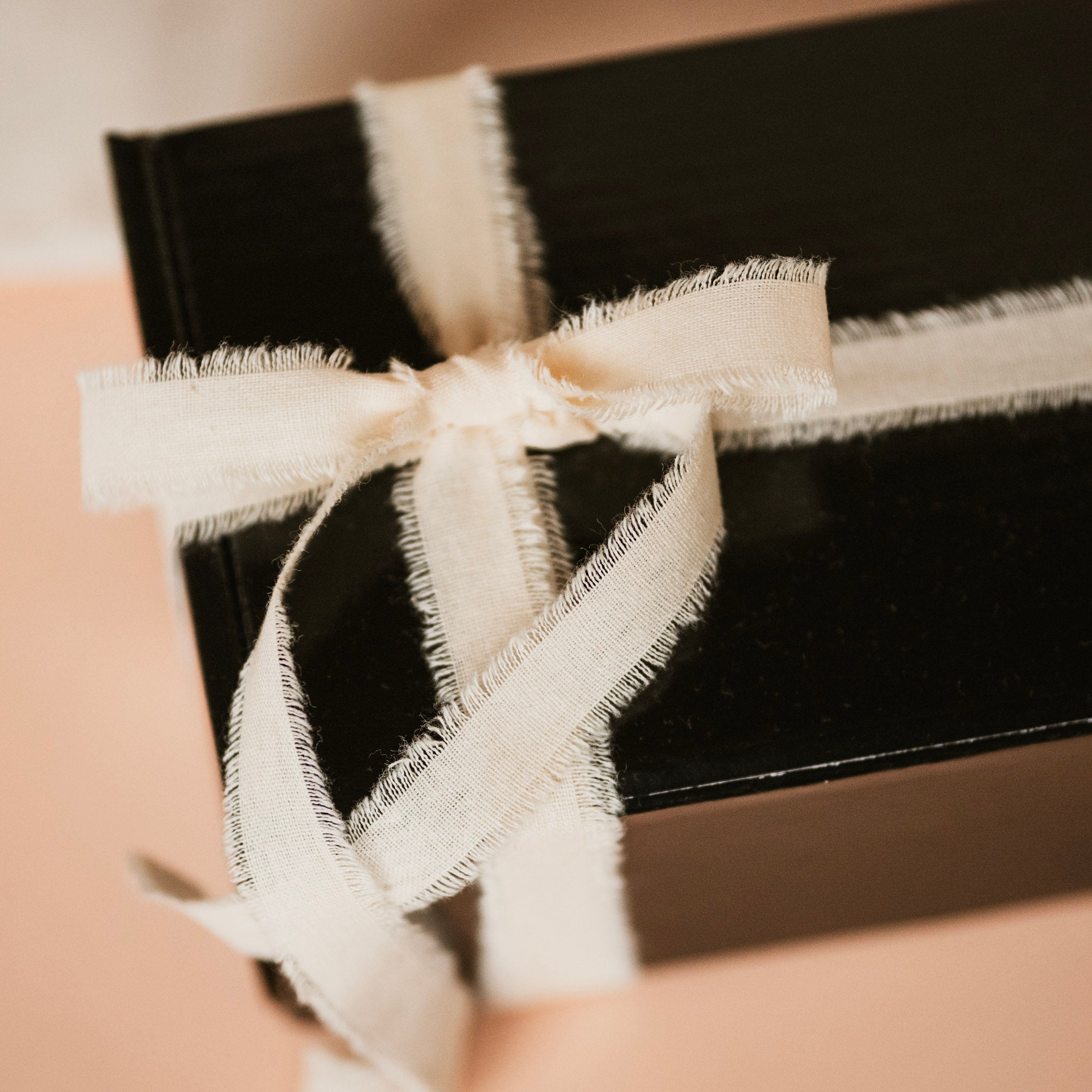 Black gift box with a white ribbon on a beige background