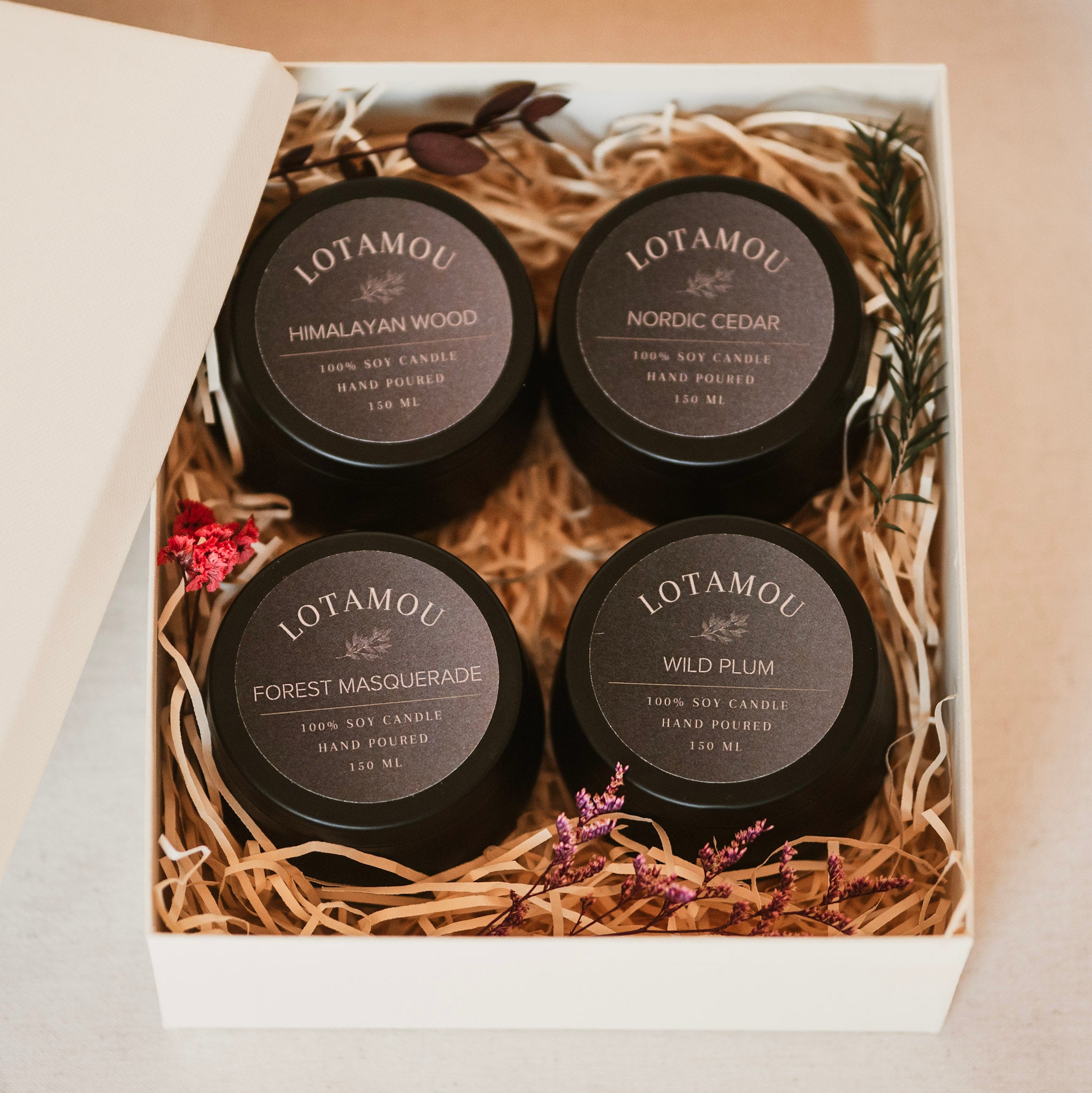 Four Lotamou candles in a decorative box with straw and flowers.