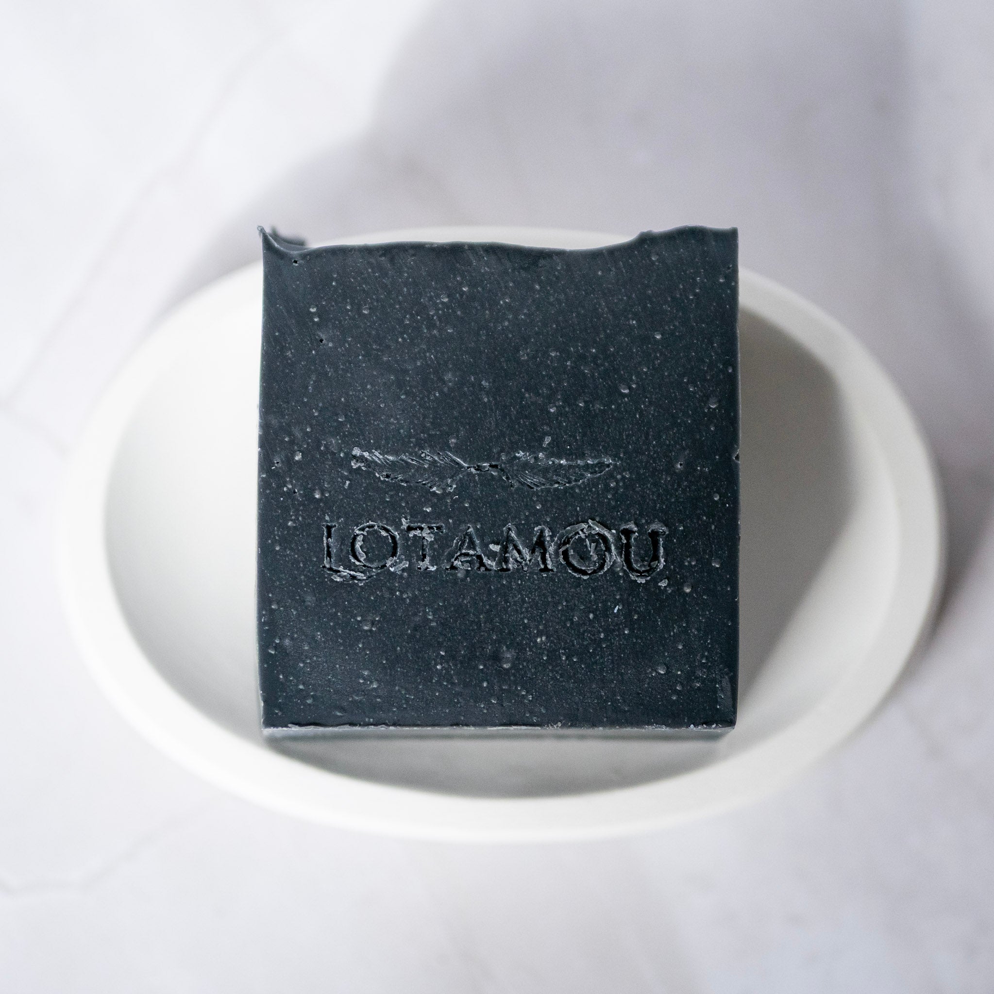 Black soap bar with 'LOTAMOU' branding on a white plate