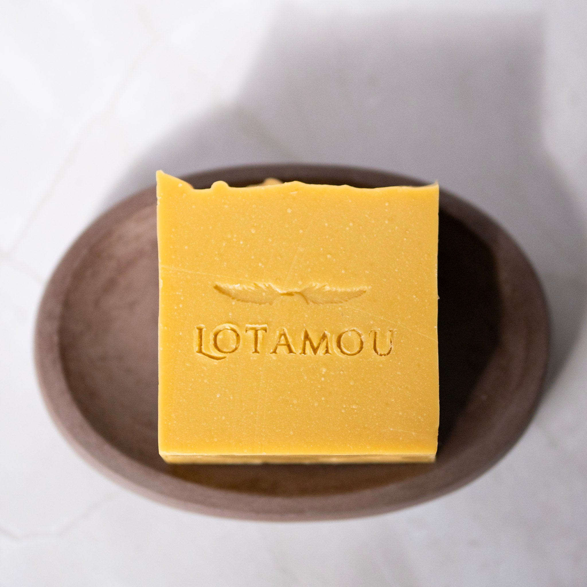 Yellow soap bar with 'LOTAMOU' branding on a dish.