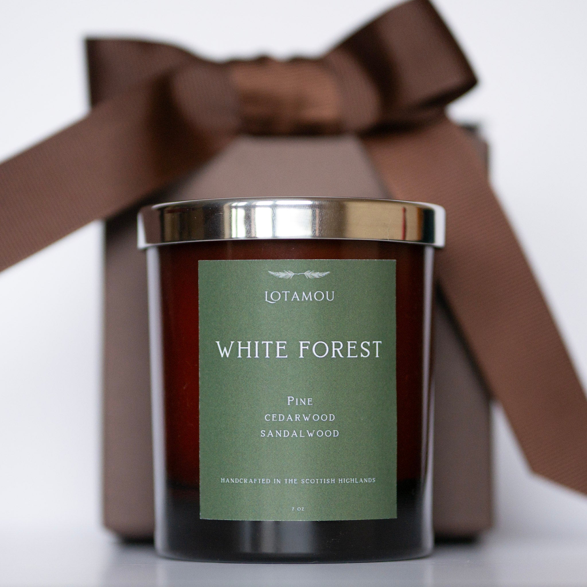 Candle with 'White Forest' label and brown ribbon on a white background