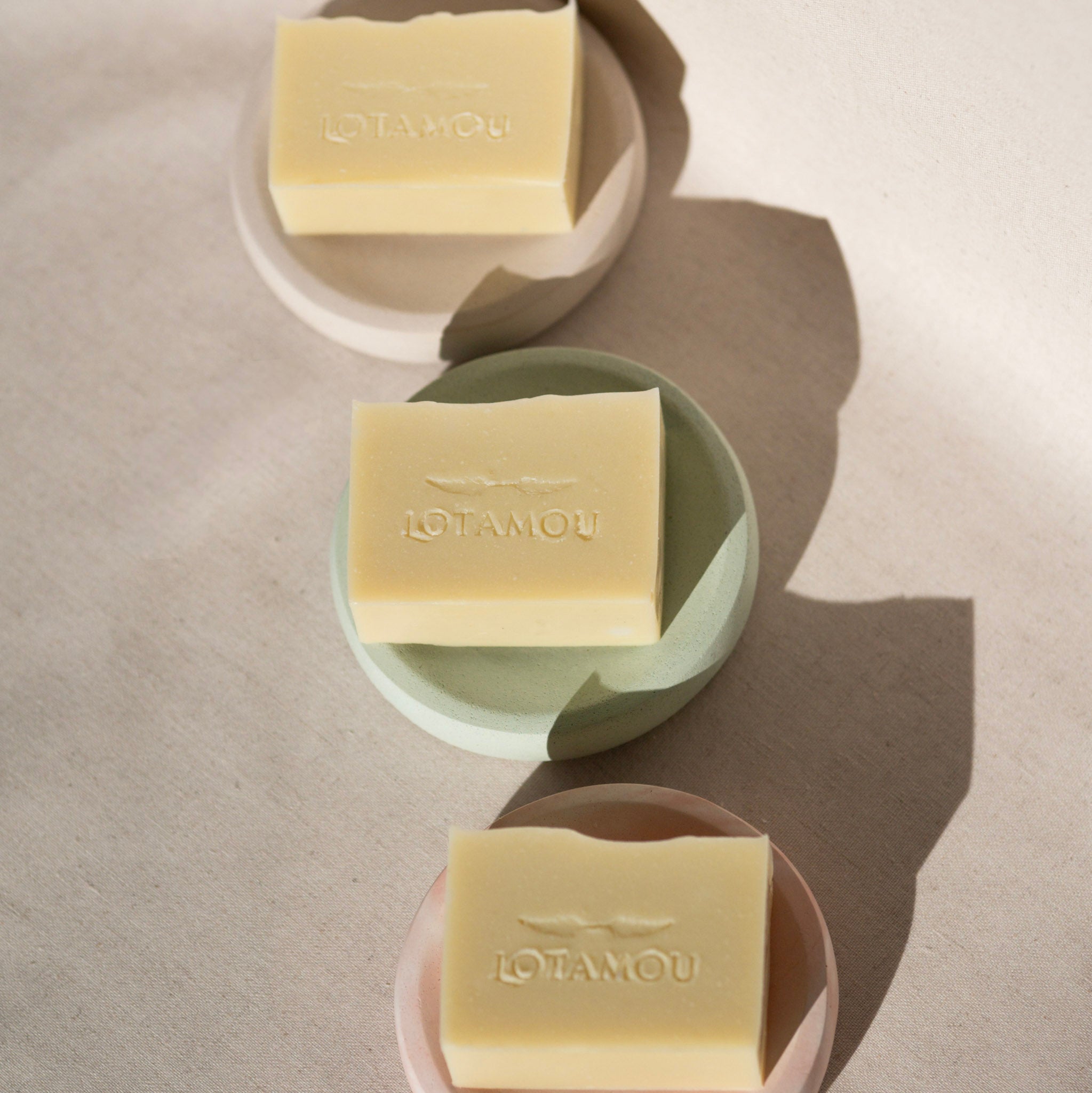 Three bars of Lotamou soap on different colored plates on a beige background
