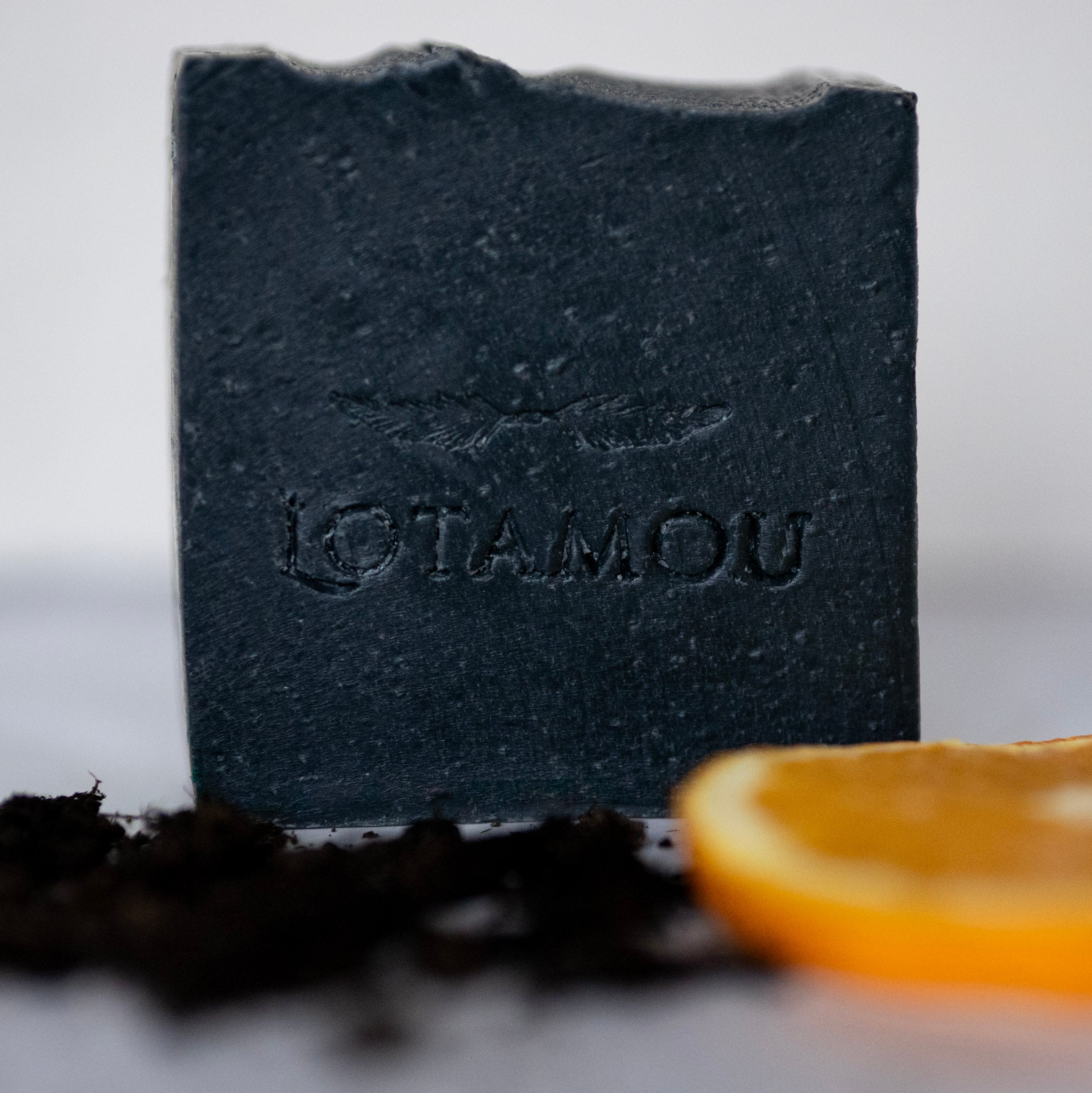 Black soap bar with 'LOTAMOU' branding next to an orange slice on a light background
