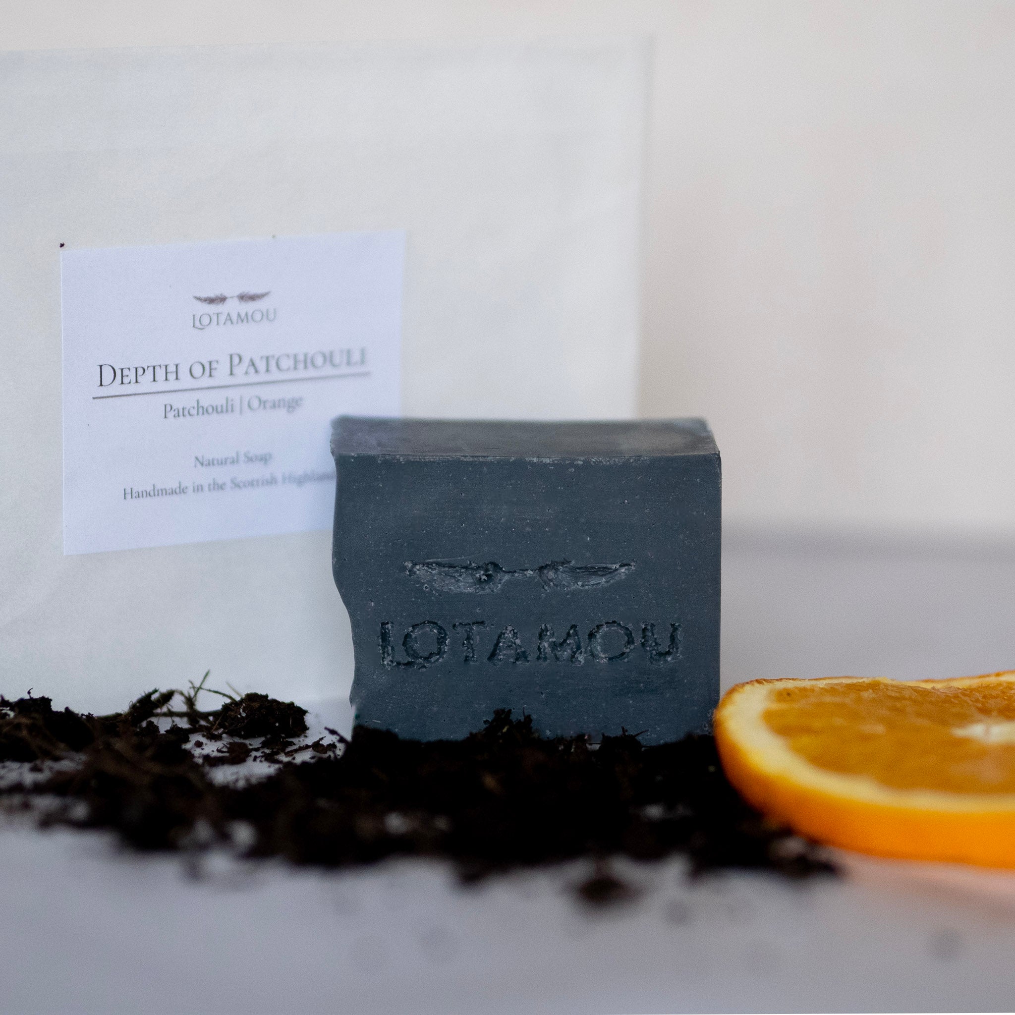 Black soap bar with 'LOTAMOU' branding, surrounded by natural elements on a light background.