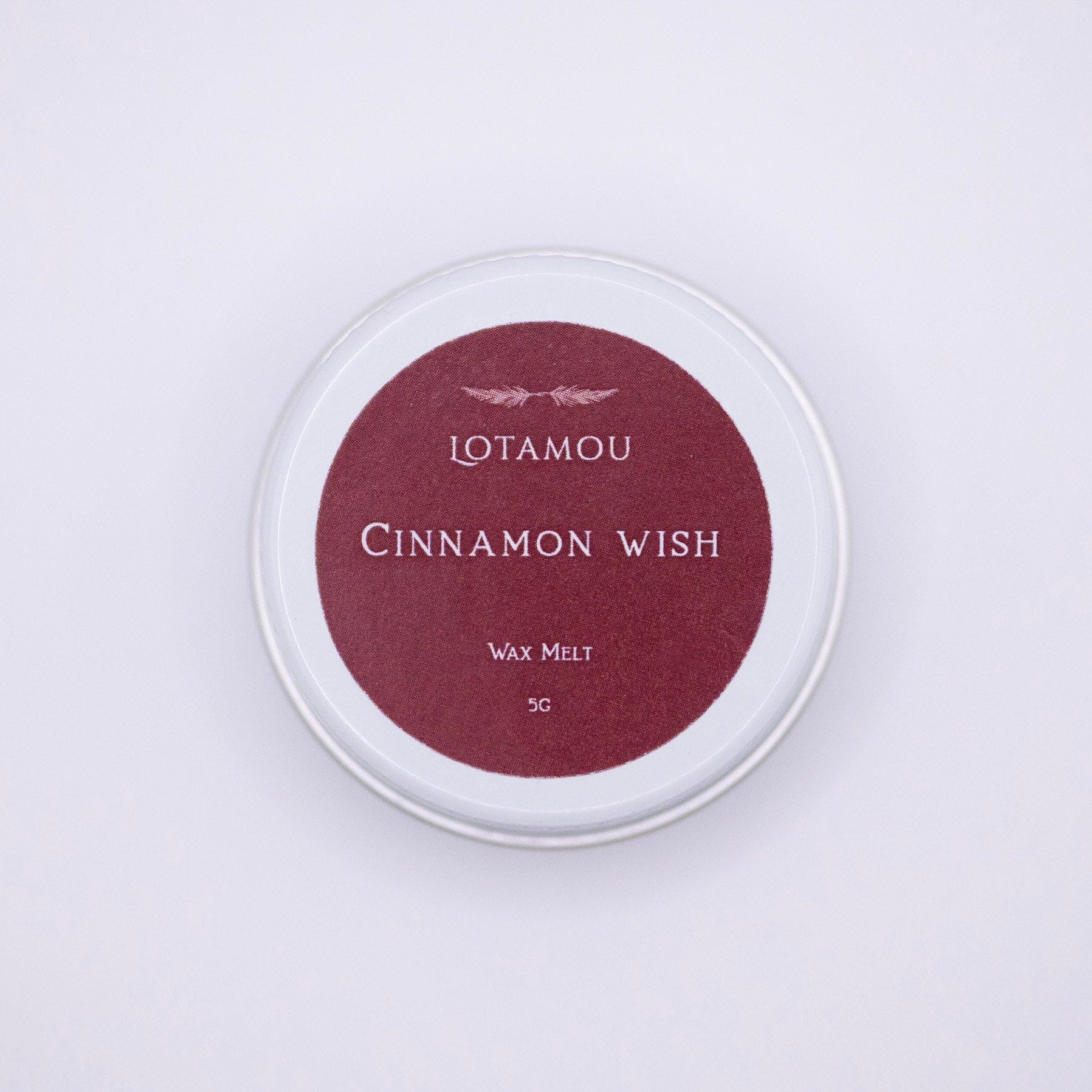 Wax melt container labeled 'Cinnamon Wish' by LOTAMOU on a light purple background