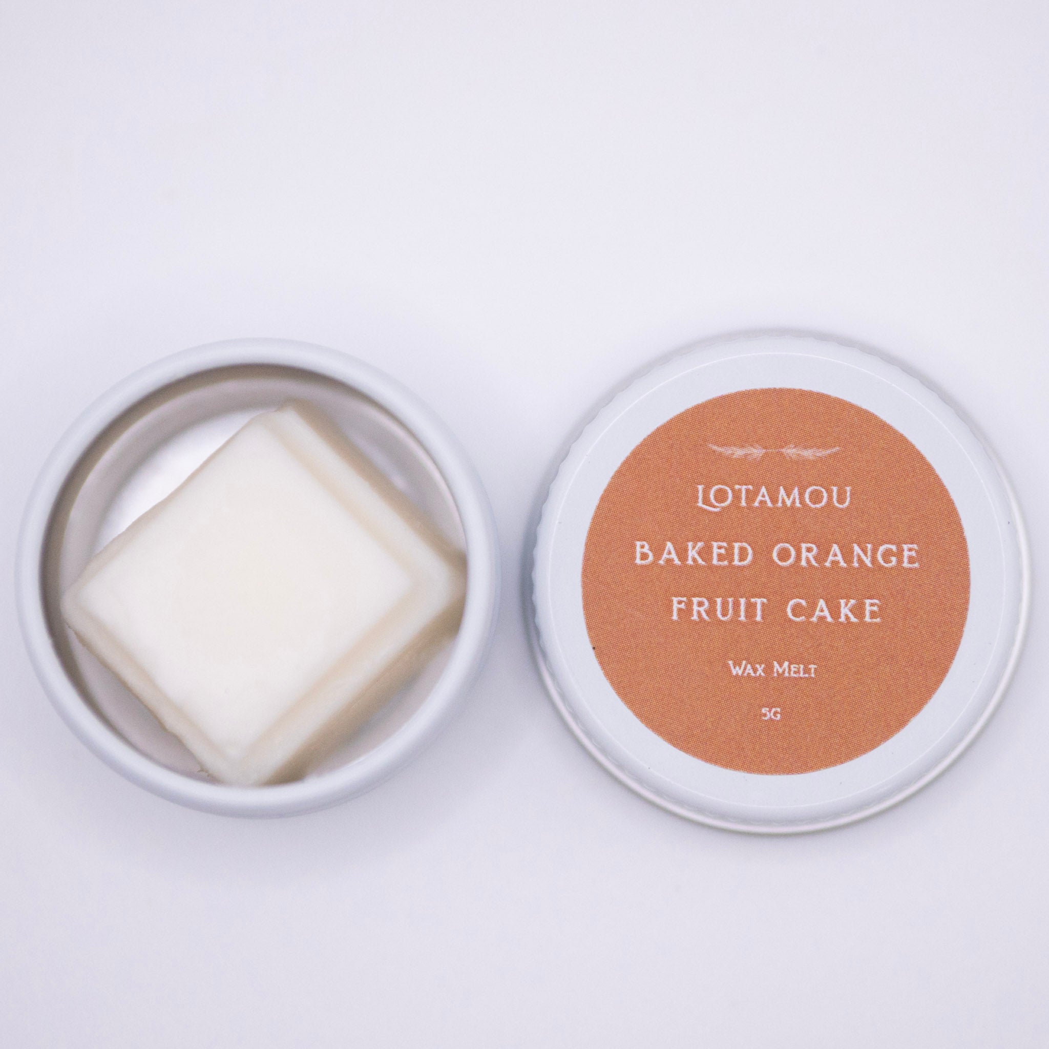Wax melt in a tin with 'LOTAMOU Baked Orange Fruit Cake' label on a white background