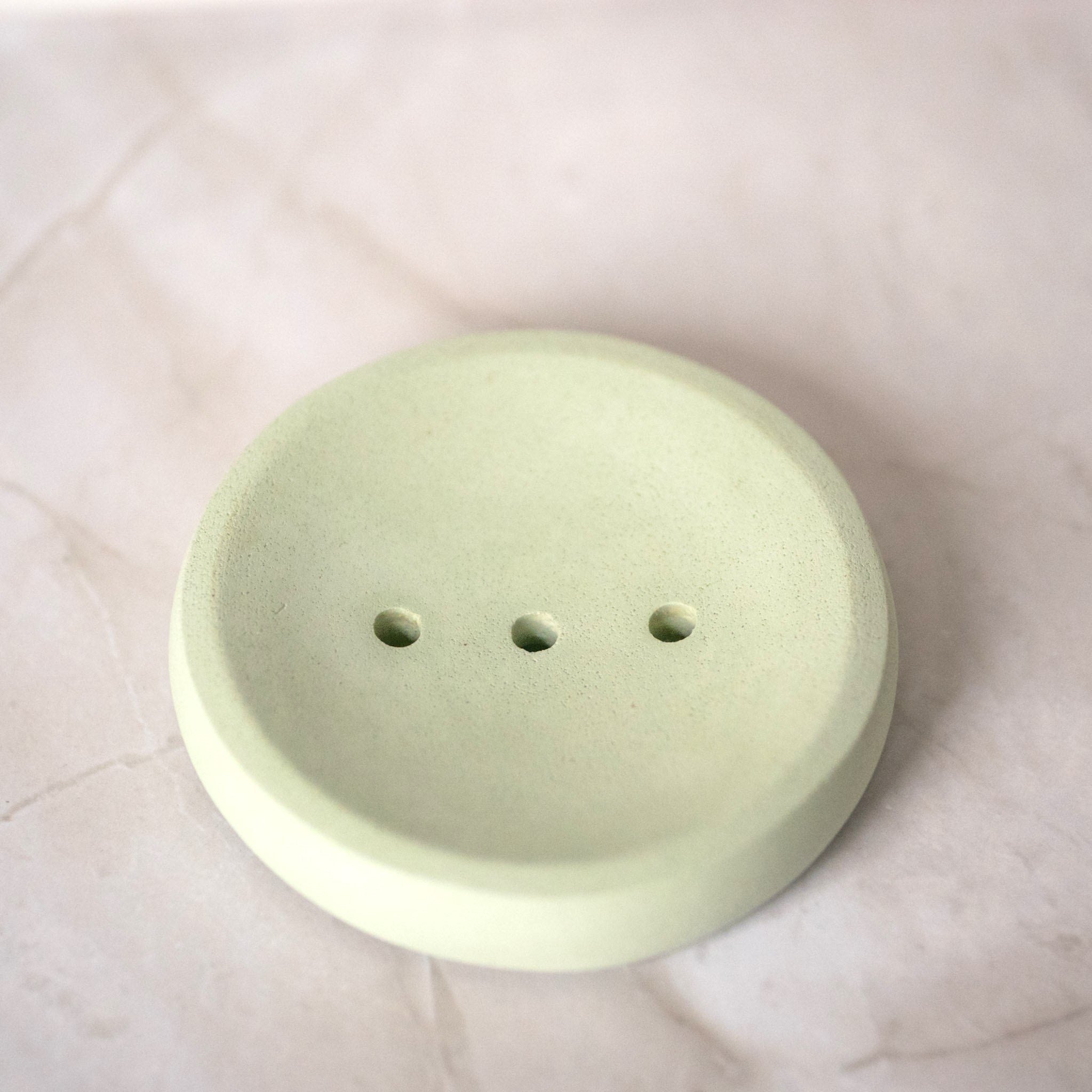 Light green ceramic soap dish with three holes on a white marble surface