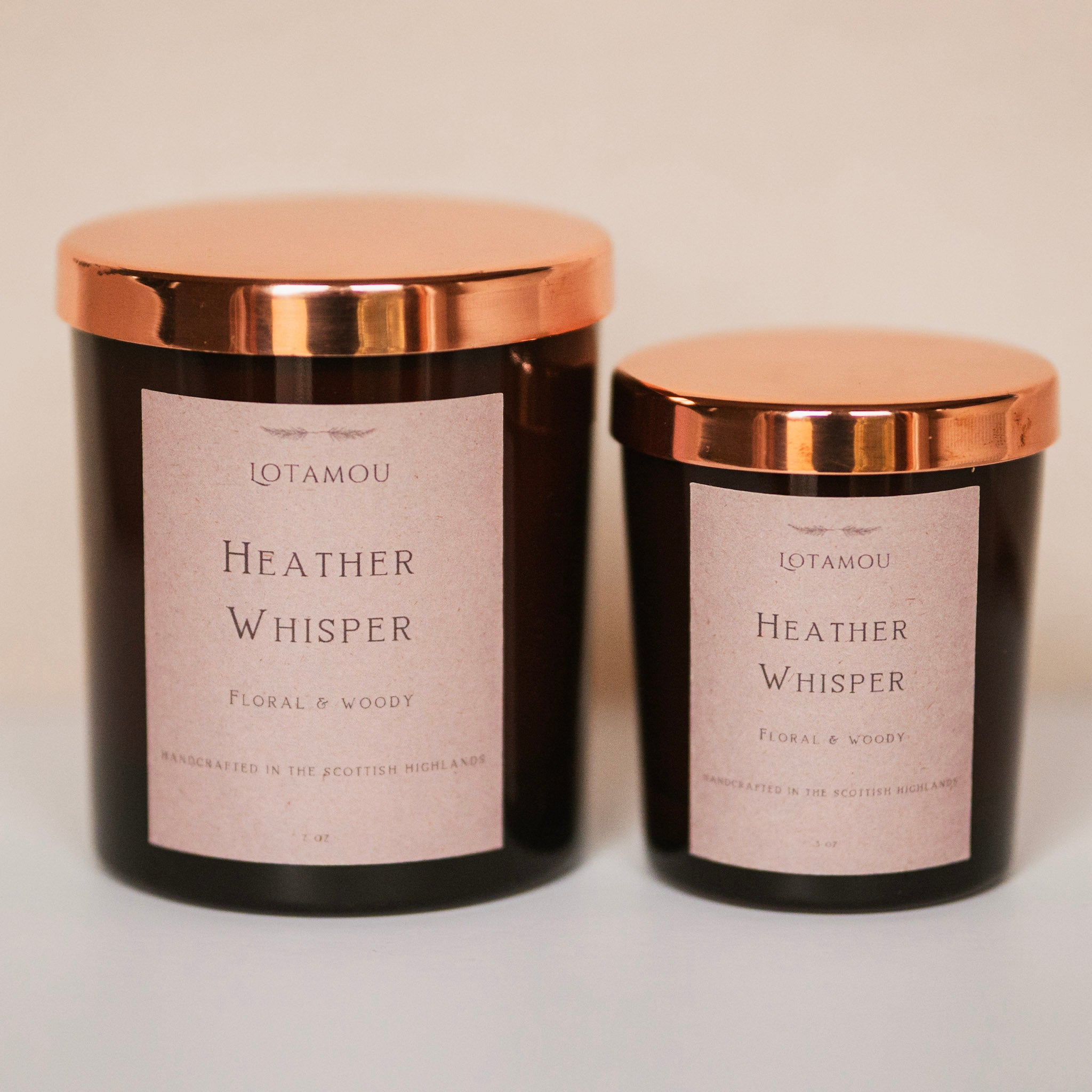 Two black candles with rose gold lids labeled 'Heather Whisper' on a light background
